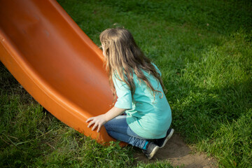 A child rides a slide in the park. The slide. Baby plays in the playground. Girl climbing a slide.