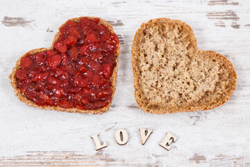 Bread in shape of heart with strawberry jam and inscription love. Rustic background