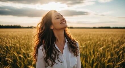 A young woman with long hair and closed eyes stands in a golden wheat field at sunset. She wears a white shirt and tilts her head back, expressing joy and freedom. Perfect for wellness content.