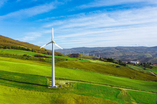 Aerial view of wind turbines integrated into a green landscape, promoting renewable energy solutions and a carbon-free strategy during the modern energy transition phase, Italy.