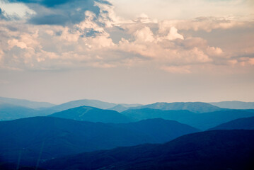 Fototapeta premium Sunset over layered mountain ridges in the Bieszczady Mountains, seen from Wielka Rawka and Mała Rawka viewpoints. Peaceful nature landscape with dramatic sky and soft evening light. 