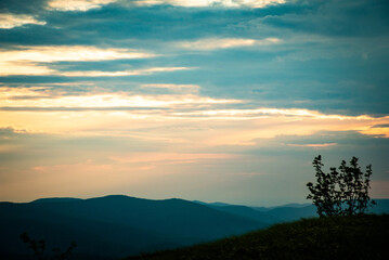 Sunset over layered mountain ridges in the Bieszczady Mountains, seen from Wielka Rawka and Mała Rawka viewpoints. Peaceful nature landscape with dramatic sky and soft evening light.
