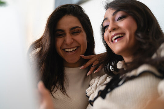 Two young women share a moment of laughter and joy, their faces illuminated by a bright light, conveying happiness and connection.