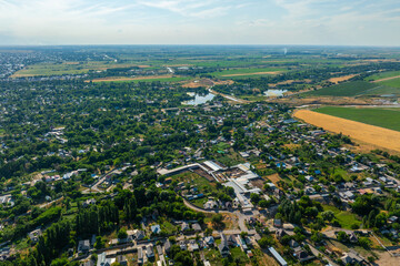 Aerial view captures serene rural flat Kyrgyzstan landscape featuring agricultural fields, houses, and a tranquil body of water. Expansive scenery showcases nature's beauty during daytime.