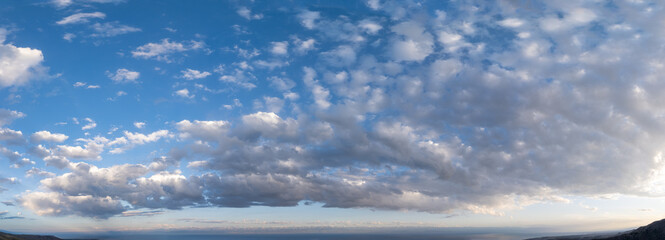 Vast serene clouds in bright blue sky over mountain covered horizon at the evening.