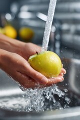 Washing a green apple under running water in a kitchen sink while preparing for a meal or snack