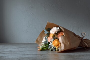 Beautiful bouquet of flowers wrapped in brown paper lies on a gray surface with a simple background