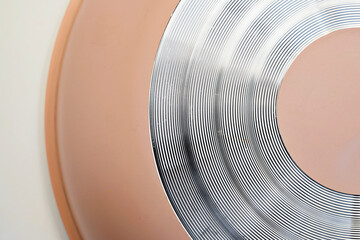 A detailed macro shot showing the bottom of a peach-colored frying pan with silver concentric circles designed for even heat distribution. Minimalist abstract kitchen background