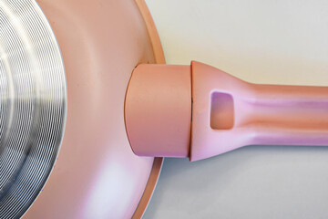 Macro shot of a modern pink non-stick frying pan showing the circular metallic induction base and...
