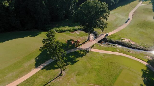 Aerial drone shot of golf cart crossing small bridge over creek on golf course path