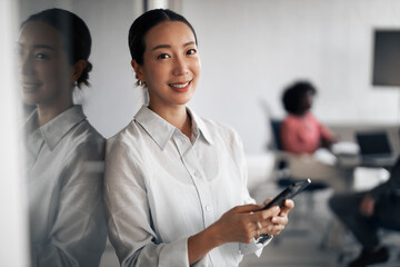 Asian business woman smiling and using smartphone in office
