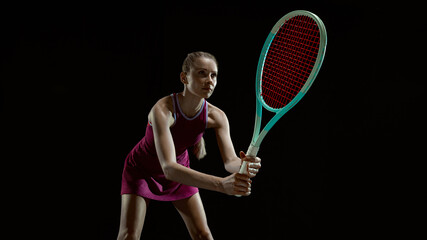 Female tennis player returning ball in dark studio with dramatic lighting. Concept of professional training, sportswear advertising, competitive focus, strength and precision in motion.