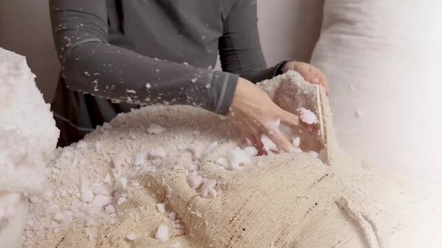 Woman fills a pillow case with foam rubber. Foam pieces, crumbs. Woman repairs furniture pillows. White polyurethane foam rubber pieces. stuffing for pillows and furniture. Cropped footage