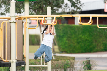 Fototapeta premium Young child playing on a playground monkey bar while smiling in a sunny outdoor park setting, showcasing joy and physical activity in childhood