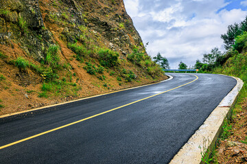 Scenic winding asphalt road curving through a steep mountain landscape under a cloudy sky.