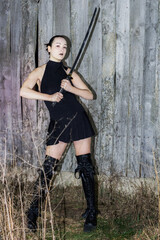 Obraz premium Cinematic outdoor portrait of woman with katana sword in black dress and dramatic lighting