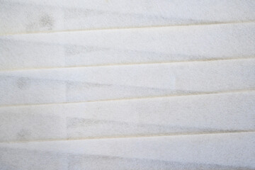A macro shot of white pleated filter material showing its fibrous texture and diagonal folds. Perfect for industrial, medical, or abstract backgrounds
