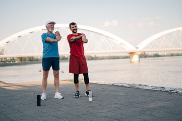 Senior man and personal trainer stretching by the river
