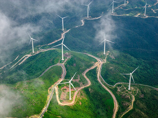 Aerial view of wind turbines generating renewable energy on green mountain ridges. © zhao dongfang