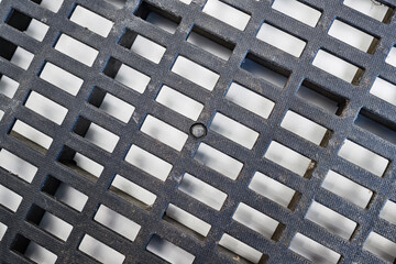 Detailed shot of a textured dark grey plastic ventilation grid with rectangular openings. The surface has a fine pattern and some dust, showing geometric industrial design