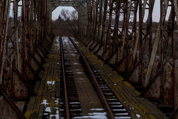 Stary, zabytkowy (dość zniszczony) most kolejowy ,z zardzewiałymi metalowymi kratownicami i drewnianymi deskami. Tory biegną przez środek, z rozproszonymi płatami śniegu na ziemi.  © Grzegorz
