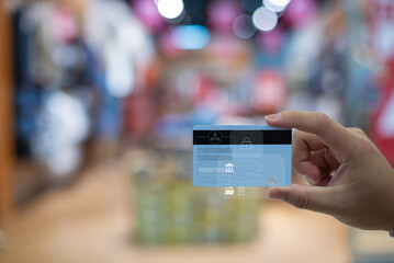 A hand holding a blue credit card with futuristic digital security overlays and cloud banking icons in a blurred shopping mall background.