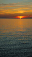 Obraz premium Golden sunset over a calm ocean with vibrant streaked clouds