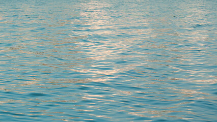 Calm teal water surface with gentle ripples reflecting golden sunset light.