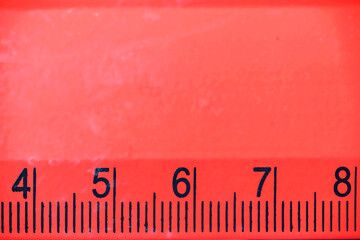 Detailed macro view of a bright red plastic ruler with black markings and numbers from four to eight. Useful for themes like back to school, math, engineering, or office supplies
