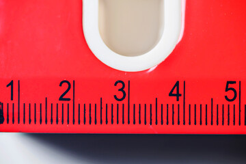 A macro close-up of a bright red plastic ruler featuring clear black measurement markings and numbers from one to five. Ideal for education, DIY, and accuracy concepts