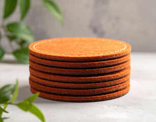 Stack of round orange felt coasters with white stitching on a textured surface