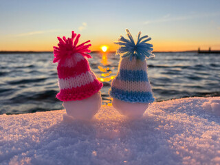 unique  snowman with knitted hats on the winter beach in sunset