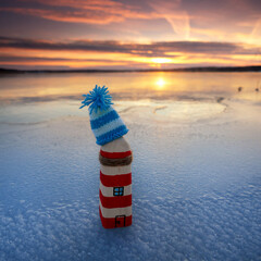 beautiful self created wooden lighthouse with knitted hat on the ice beach in winter