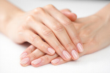 Closeup of manicured female hands with pink nails on white surface