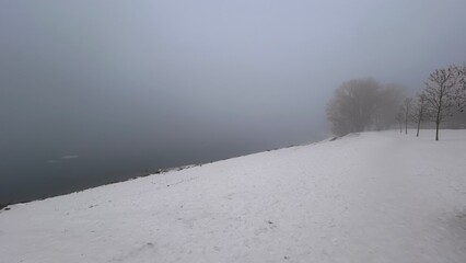 Snowy foggy river shore covered with plain snow. Monochrome nature.