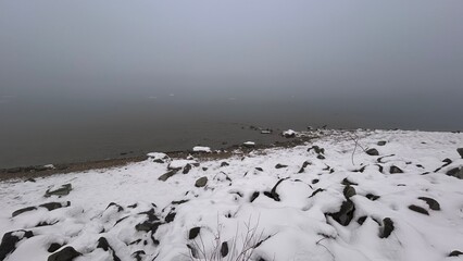 Snowy foggy river shore. Winter romantic landscape. Monochrome arctic nature.