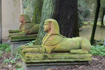 Pair of moss-covered sphinx statues beside a tree in the Egyptian area of Stibbert Park, a 19th-century English garden in Florence, Italy.
