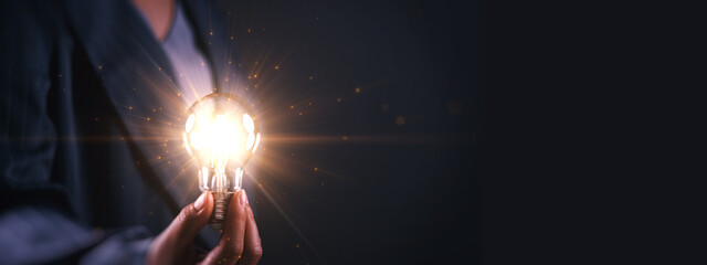 Innovation concept with a glowing light bulb held by a business professional on dark background, symbolizing creative ideas, inspiration, problem solving, leadership, strategy, and thinking business.
