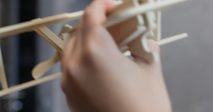 Little child hand holds wooden airplane model playing at home closeup. Active kid carries vintage plane made of wooden constructor POV. Imagination development