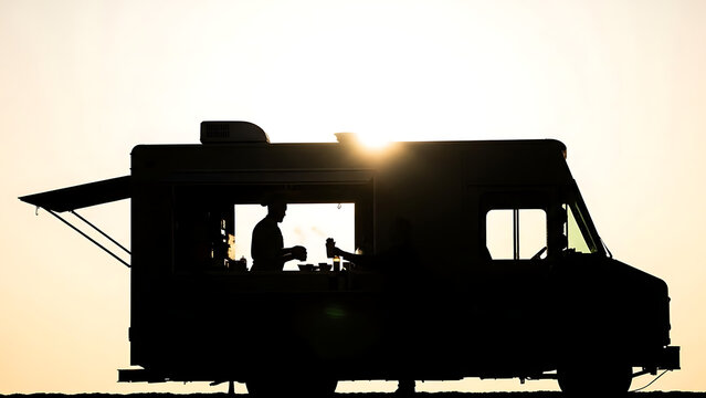 Silhouette of food truck at sunset with chef preparing meal - Powered by Adobe