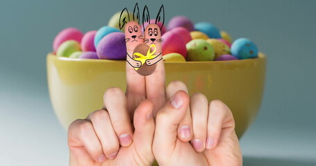 Image of fingers with easter bunnies and easter egg over bowl of easter eggs on blue background
