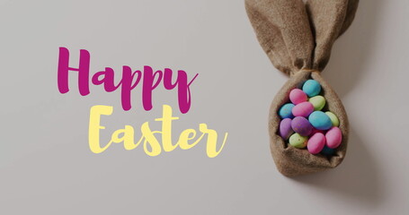 Image of happy easter text over colourful easter eggs in cloth on grey background