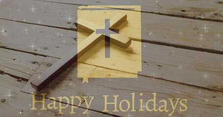 Image of happy holidays text over christian cross on wooden background