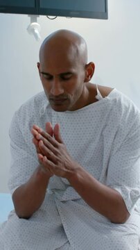 Vertical video: Closing eyes patient in gown rubbing palms and cupping head on exam table calming