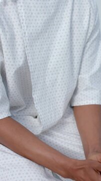 Vertical video: Pullback showing man in gown moving hands turning head waiting for scan in clinic