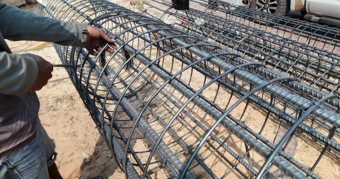 close up of a construction worker tying a steel rebar cage together with wire and a hand tool.