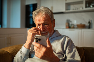 Senior man crying while looking at smartphone at home