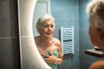 Senior woman wrapped in towel looking in bathroom mirror