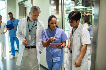 Doctors and nurse collaborating with tablet in hospital corridor