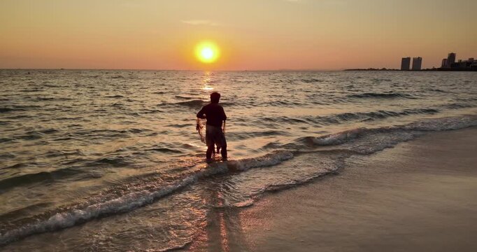 Fisherman standing in the surf and casting his net into the sea at sunset. ( In slow motion )